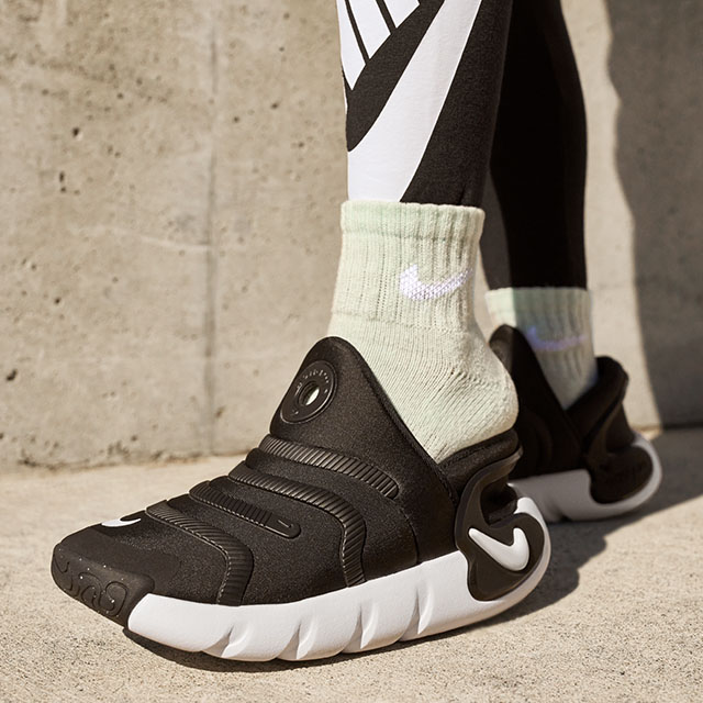 Person stepping into black Nike Easy On slip-on shoes with a sculpted white sole.